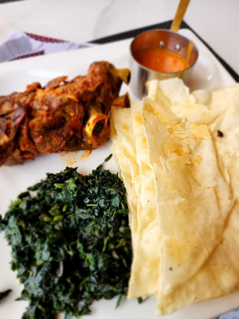 slow-cooked spicy goat with dodo with naan bread and spicy peanut sauce. The Hut Kigali Rwanda 